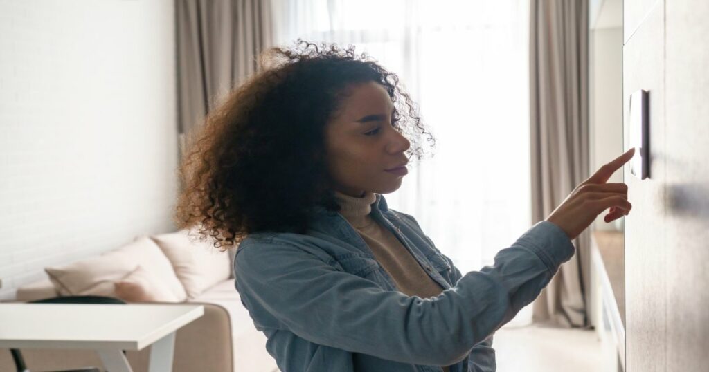 A woman adjusts her HVAC zoning system temperature on a thermostat