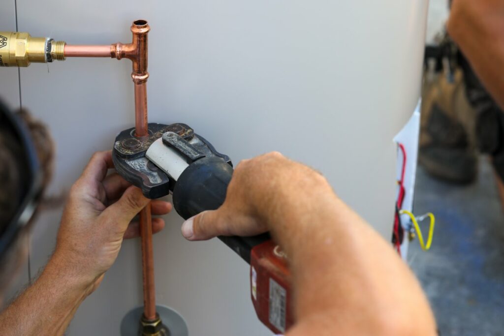 A close up of a plumber installing an electrical hot water cylinder